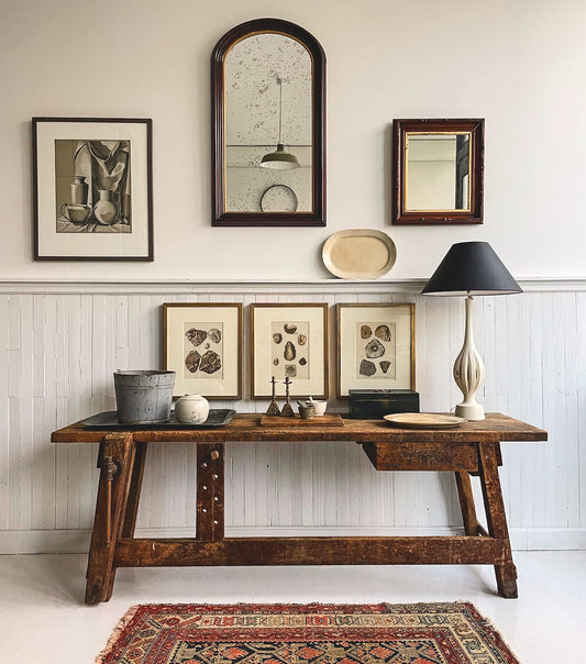 A curated interior showcasing antique and contemporary art on a gallery wall with vintage furniture below.