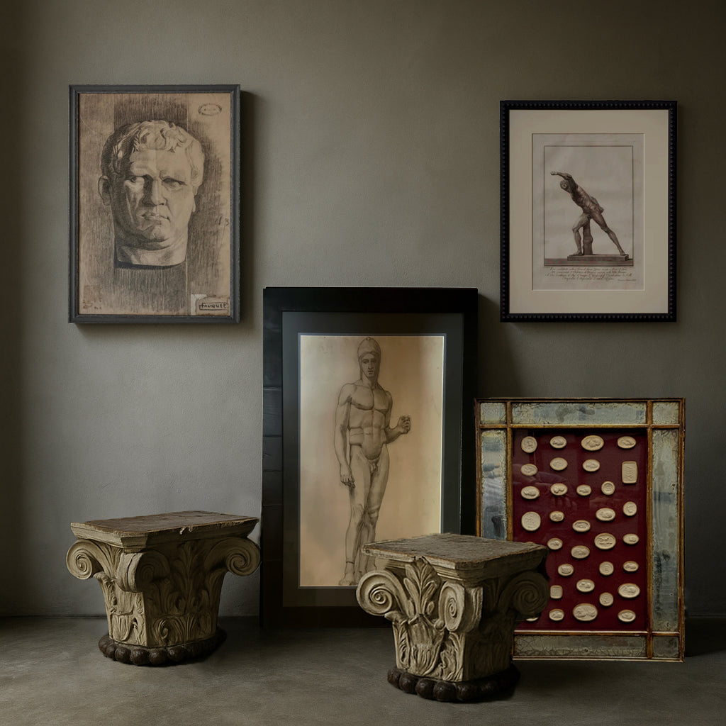 Framed classical drawings, antique intaglios, and architectural capitals arranged in a curated neoclassical art collection