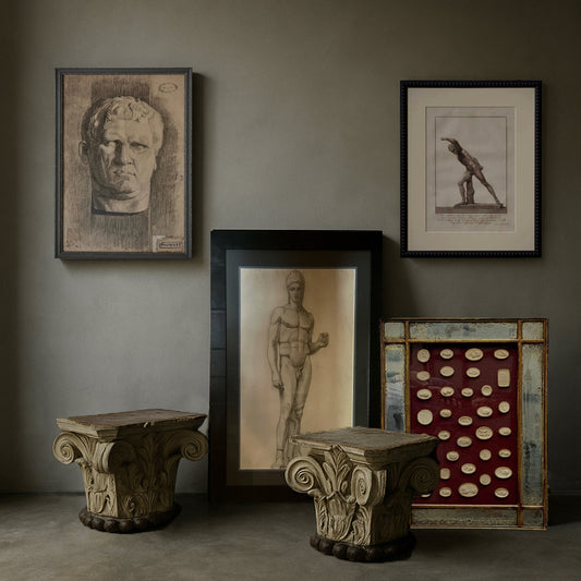 Framed classical drawings, antique intaglios, and architectural capitals arranged in a curated neoclassical art collection