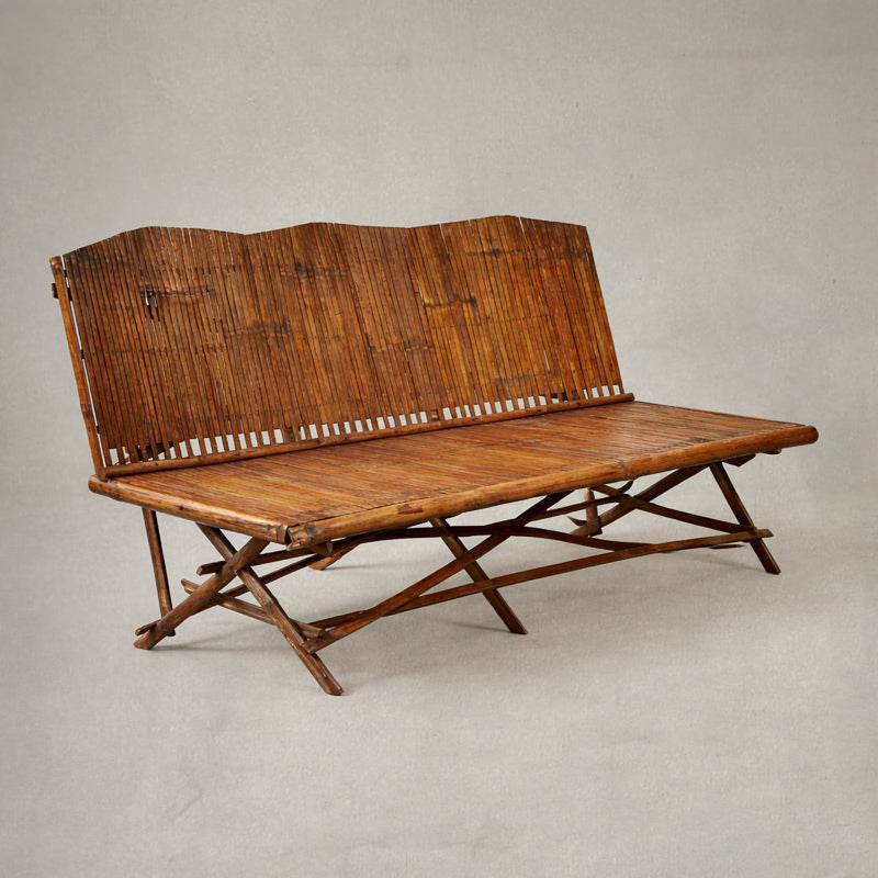 1920s English bamboo bench with slatted back and seat, shown against a soft neutral background, highlighting warm patina and folding base structure. left side view