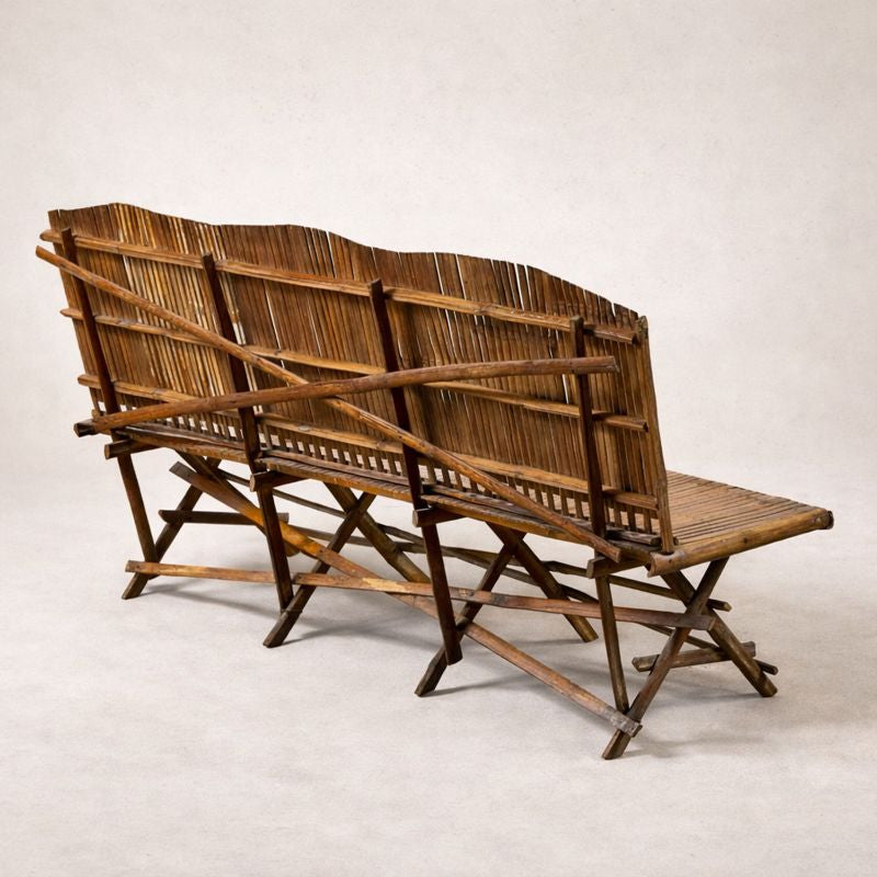 1920s English bamboo bench with slatted back and seat, shown against a soft neutral background, highlighting warm patina and folding base structure. back side