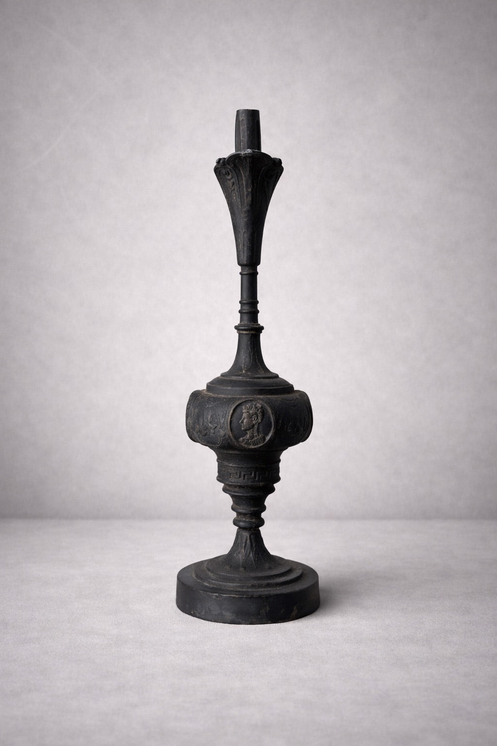 Alternate rear angle of classical metal ewer highlighting sculptural silhouette and aged patina on gray surface