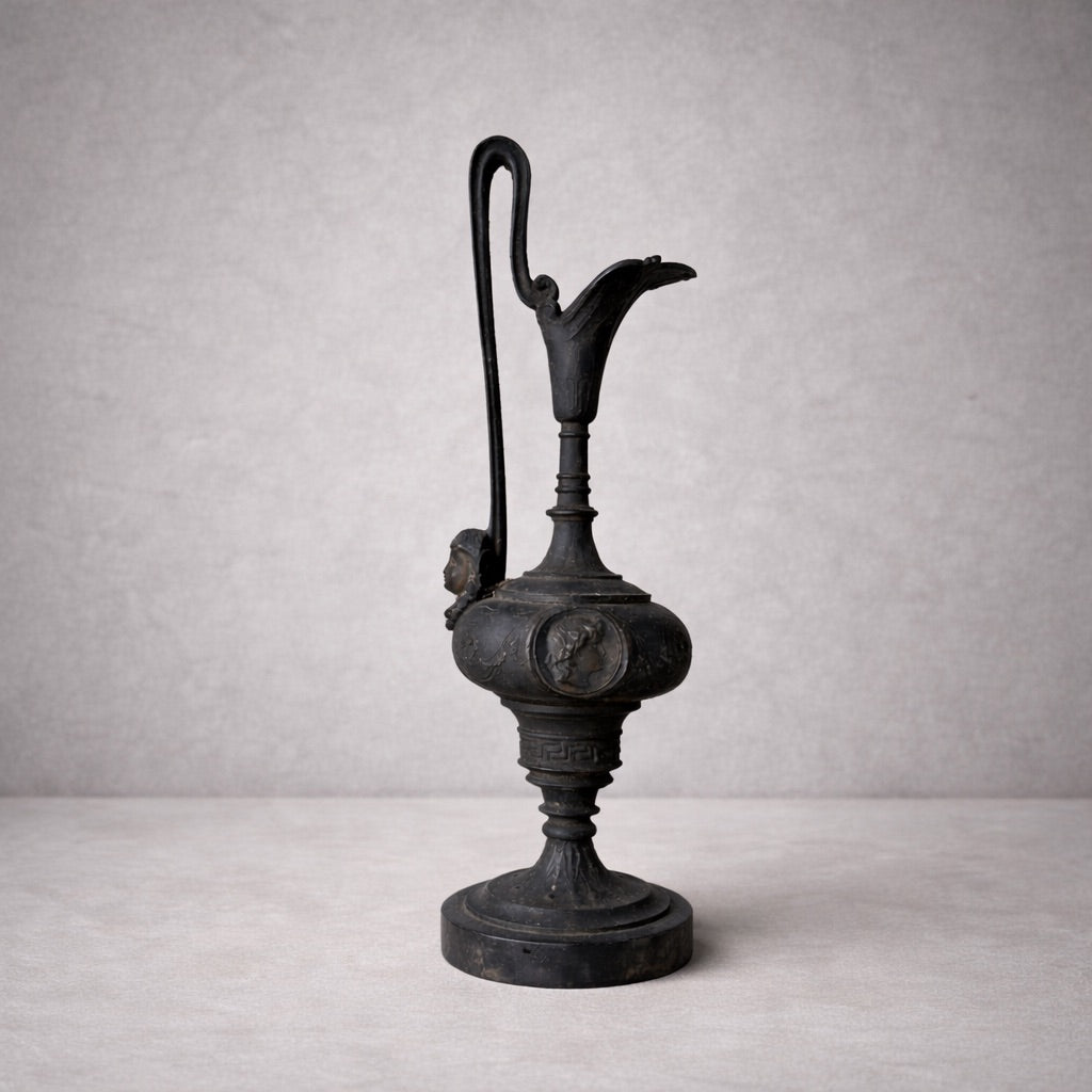 Neoclassical cast metal ewer with tall handle and classical relief medallions on neutral background