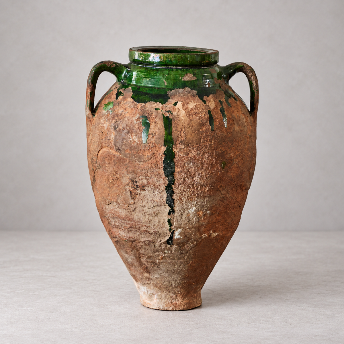 Two-handled terracotta olive oil pot with patchy green glaze, exposed textured clay, and a narrow base.