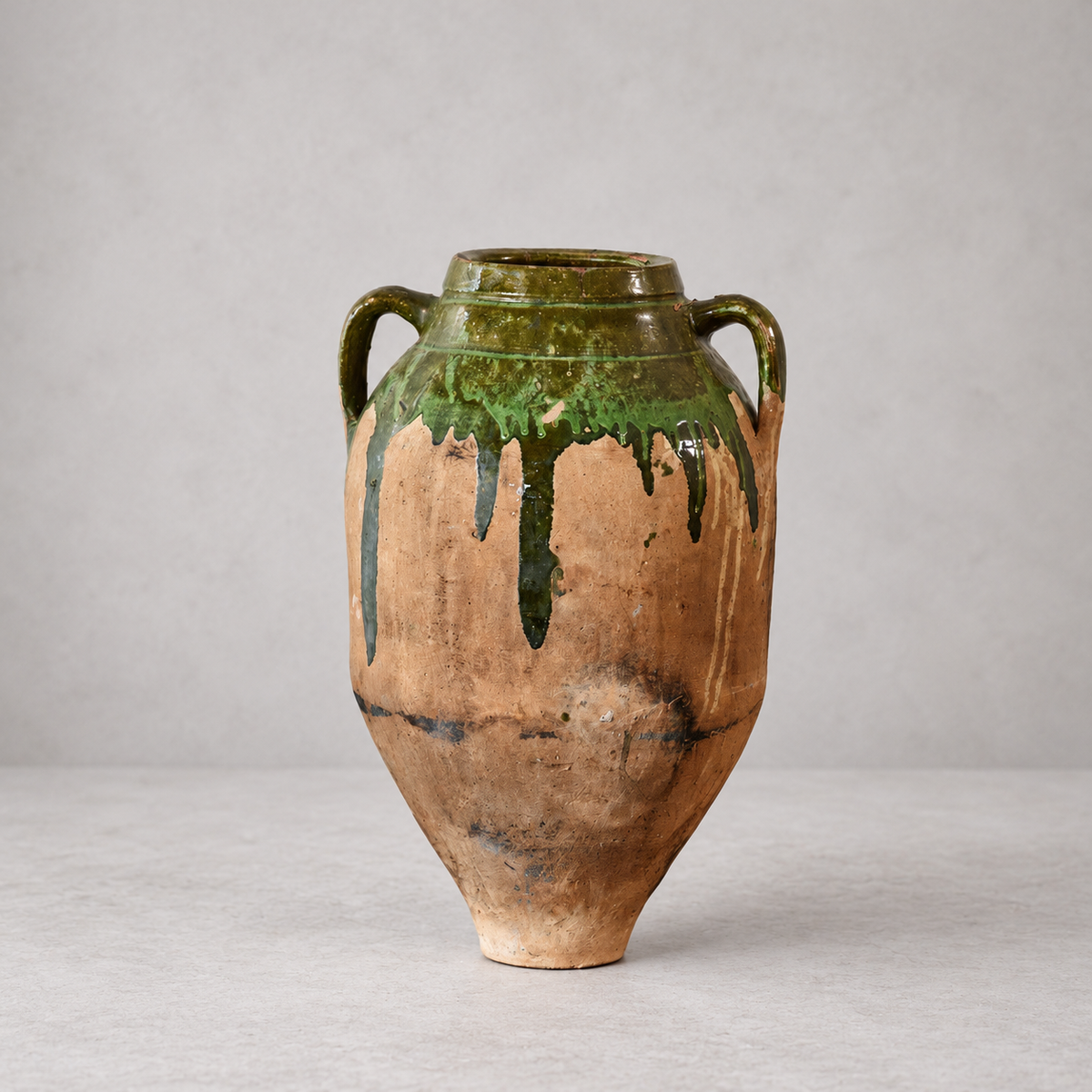 Antique Bulgarian terracotta olive oil pot with two handles, long green glaze drips, and dark wear across its tapered body.