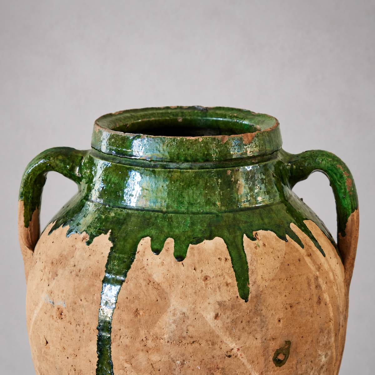 Detail of a Bulgarian terracotta pot with two curved handles, a chipped rim, and green glaze running over pale clay.