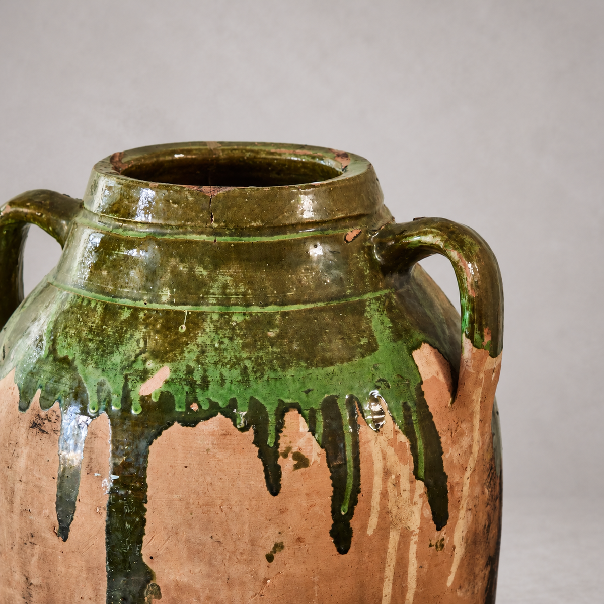 Close-up of an olive oil pot’s olive-green glazed neck and handle, showing a fine rim crack and exposed terracotta chips.