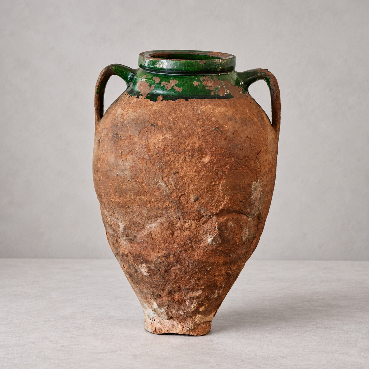 Reverse of an antique terracotta olive oil pot, showing rough reddish clay, surface wear, and green glaze around the neck.