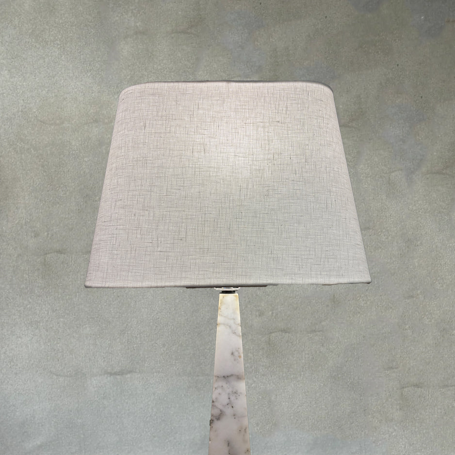 Top half detail of midcentury Italian white Carrara marble table lamps with geometric bases and ivory linen shades on a neutral textured backdrop