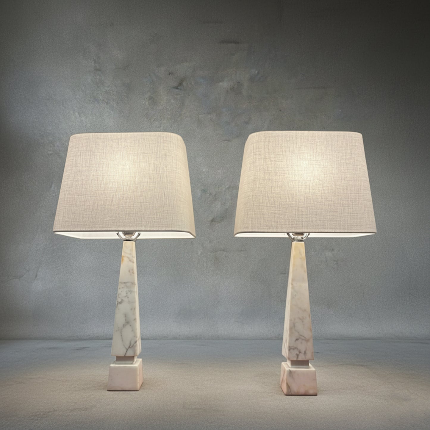Pair of midcentury Italian white Carrara marble table lamps with geometric bases and ivory linen shades on a neutral textured backdrop