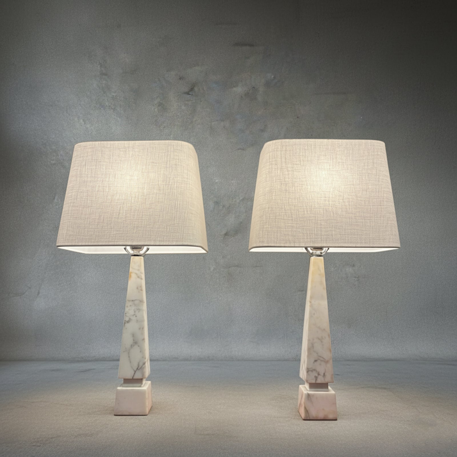 Pair of midcentury Italian white Carrara marble table lamps with geometric bases and ivory linen shades on a neutral textured backdrop