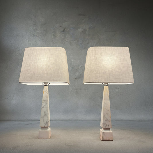 Pair of midcentury Italian white Carrara marble table lamps with geometric bases and ivory linen shades on a neutral textured backdrop